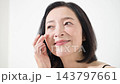 A middle-aged Japanese woman smiles while checking the wrinkles around her eyes; an image of anti-aging care and skincare for women in their 50s. 143797661