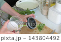 At a kitchen counter, a woman soaks leafy vegetables in water with baking soda to remove pesticides, preparing them for washing and use 143804492