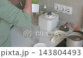 At a kitchen counter, a person adds cucumber, celery, chia seeds, and plant-based milk to a blender to prepare a smoothie 143804493