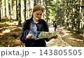Young woman hiker holding and reading paper map in forest 143805505