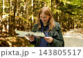 Smiling woman hiker checking paper map on a forest trail 143805517