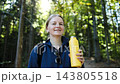 Smiling woman hiker with a yellow thermos looking at camera in forest 143805518