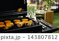 Close up of corncob and breaded patties grilling on open barbecue with blurred rooftop lights behind, illustrating outdoor cooking, cookout food and casual event. 143807812