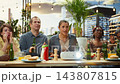 Friends gesturing with tense expressions around video projector while watching sports match at rooftop barbecue, illustrating suspense, debate and shared fan engagement. 143807815