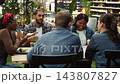 Group of friends talking and laughing across rooftop dining table with food and beer bottles supporting casual entertaining and fun group conversation. Entertaining BBQ party. 143807827