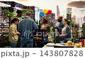 Cheerful group of friends clinking beer bottles in celebratory toast near rooftop barbecue grill while men cook food, corn and patties during outdoor party and social gathering. 143807828