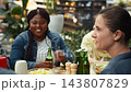 Woman holding beer bottle for cheers gesture with friends around dining table, talking and laughing together at rooftop barbecue party. Toast with alcohol. 143807829