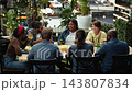 Group raising drinks for rooftop barbecue toast around outdoor table, celebrating with beer bottles at BBQ party. Socializing, shared meals and relaxed urban leisure. 143807834