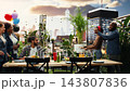 Group of friends revealing birthday surprise for woman with eyes covered, people gathered around barbecue table for rooftop party. Celebration and socializing with drinks and food. 143807836