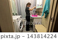 Woman cleans hands in basin. Woman thoroughly washes her hands using pink basin in warm bathroom. Lady carefully cleans her hands in vibrant pink basin within cozy bathing environment 143814224