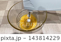 Whisking eggs vigorously. Egg mixture being frothy quickly. Electric mixer rapidly transforms eggs into frothy foam. Fast spinning electric whisk produces frothy bubbles from eggs in glass bowl 143814229