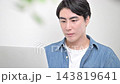 A young Japanese man typing on a laptop keyboard in the brightly lit interior of his home. 143819641