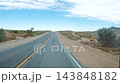 Vehicle driving along empty paved highway through arid desert landscape under bright sunny sky, offering front pov motion view of scenic route journey 143848182