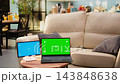 Blue screen and green screen mockup on coffee table in living room, warm tones and gadgets highlighting modern interior design bright details. Editable screen. 143848638
