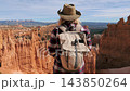 Female hiker wearing a backpack and hat standing on cliff edge, admiring red rock hoodoos of bryce canyon national park during an outdoor adventure. Camera panning around standing hiker on top canyon 143850264