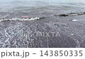 Plastic trash and floating garbage washing ashore on dark sandy beach dirty ocean water environmental pollution problem 143850335
