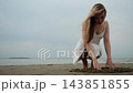 Young Woman in White Dress Touching Sand on Beach. 143851855