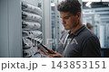 Male Network Technician Verifying Patch Panel Connections with Tablet Reference 143853151