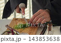 Hands chopping green herbs with a chef knife on a wooden board 143853638