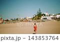 Woman jogging barefoot toward and away from the camera in a red swimsuit 143853764