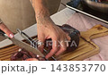 Hands cutting octopus tentacles with a knife and kitchen tongs 143853770