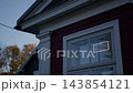 Red house exterior with glowing open sign in window at dusk, framed by white trim and autumn trees near blue evening sky 143854121