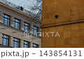 Modern urban building facades with golden wall panels, rows of windows, bare tree branches, and clear daylight sky over 143854131