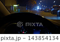 Driver view inside car at night with glowing dashboard, steering wheel foreground, and blurred city street lights beyond 143854134