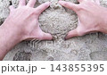 Close-up top view of man hands kneading and squeezing handful of grainy crumbly sand mass on sandy beach. Top-down POV of male hand mixing sand material. Construction work or leisure activity theme. 143855395