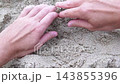 Close-up top view of male hands digging, scooping up and holding handful of textured wet grainy sand on sandy beach. Top-down POV of man hand touching sandy surface. Summer vacation holiday theme. 143855396