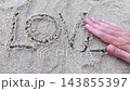 Close-up top view of man hands wiping out word LOVE on sand surface and then drawing by fingers heart shape symbol on sandy beach. Summer vacation and romantic love confession or breakup concept theme 143855397
