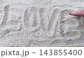 Close-up top view of male hand writing by finger word LOVE on white clean sand surface on sandy beach. Top-down first person POV of man hands. Summer vacation holiday and romantic confession theme. 143855400