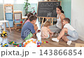 Attentive woman teacher explaining and telling to children of different ages, writing on blackboard during lesson at classes for kids 143866854