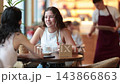 Two European women sitting at a table in a bright cafe, chatting and drinking hot coffee made from Arabica beans 143866863