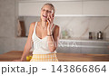 Smiling young woman in summer shorts speaking on mobile phone in kitchen during daytime  143866864