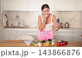 Young woman preparing salad and looking at smartphone in kitchen  143866876