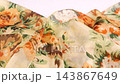 A piece of silk fabric with a floral pattern drops gently onto a white background. This detailed slow motion shot captures the elegant folds of light orange and green textile. 143867649