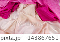 A vibrant red silk fabric falls in slow motion onto a soft cream and light pink textile background. This multi-colored drapery creates elegant layers ideal for luxury fashion and modern apparel design 143867651