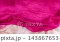 Pink silk fabric falls smoothly in slow motion onto bright textiles. This soft flowing material creates elegant waves and luxurious pink folds.  143867653