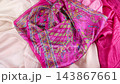 Pink silk shawl with a traditional paisley pattern falls in slow motion onto layered luxury fabrics. This vibrant fuchsia and emerald green textile beautifully demonstrates the soft texture. 143867661