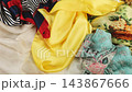 Beautiful silk scarfs with traditional floral and geometric patterns are elegantly stacked together. A soft yellow silk fabric gently falls over the colorful textiles in slow motion.  143867666