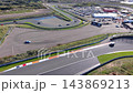 High angle aerial view of race track straight with sports cars orange kerbs pit lane entry event marquees paddock and coastal sand dunes at Circuit Zandvoort in North Holland Netherlands 143869213