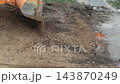 Orange excavator bucket emptying loose earth and gravel onto ground, creating pile of construction debris during excavation work on a development site, slow motion, copy space 143870249