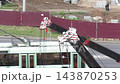 Crane booms with cables and pulleys extend over a busy street, construction site in background, workers and material, industrial development and urban infrastructure project 143870253