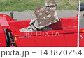 Loading of construction debris into red dump truck container. Heavy machinery operation for waste removal from building site. Process of demolition material transport for disposal. 143870254