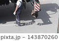 Worker stands on asphalt surface next to construction equipment, body obscured by machinery shadow, preparing for task, focus on safety gear and heavy vehicle components, daytime outdoor scene, 143870260