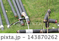 Black insulated pipes with red caps and white bands lifted by crane straps for underground utility installation project on green grassy ground during daytime construction work 143870262