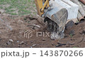 Excavator bucket digging up earth and broken asphalt on construction site during demolition work for infrastructure repair, exposing manhole cover and underground pipes 143870266