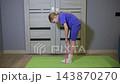 Young girl performing bending exercise with resistance band at home, standing on green fitness mat, demonstrating dedication to physical activity and healthy lifestyle practice indoors 143870270