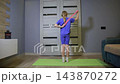 Young girl performs arm stretch with resistance band on yoga mat in living room. Fitness activity for child physical development at home, back view. 143870272